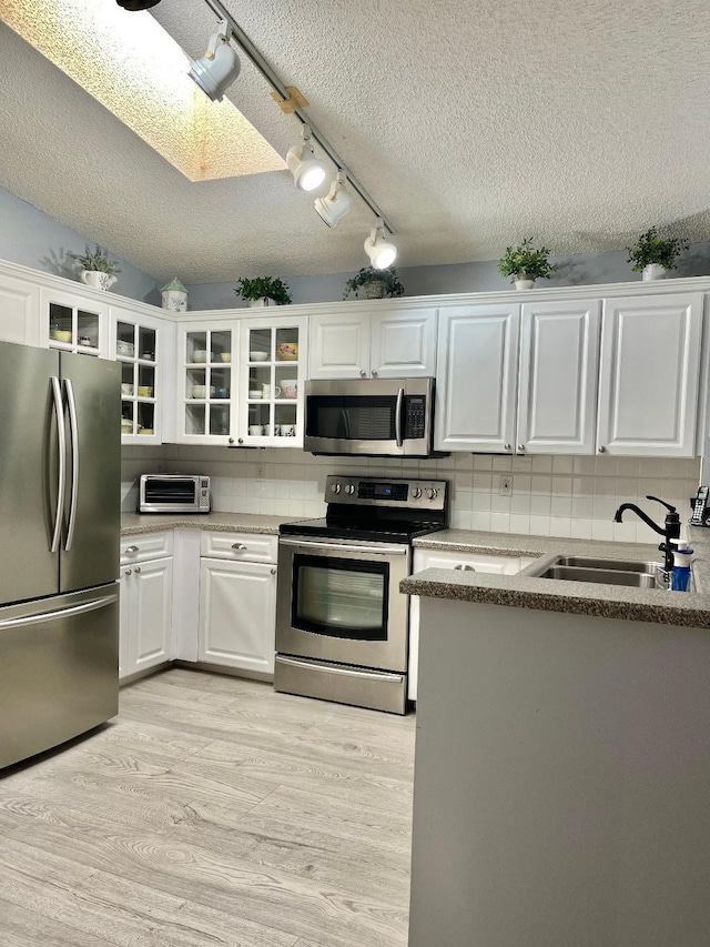 kitchen featuring light hardwood / wood-style floors, stainless steel appliances, white cabinets, sink, and backsplash