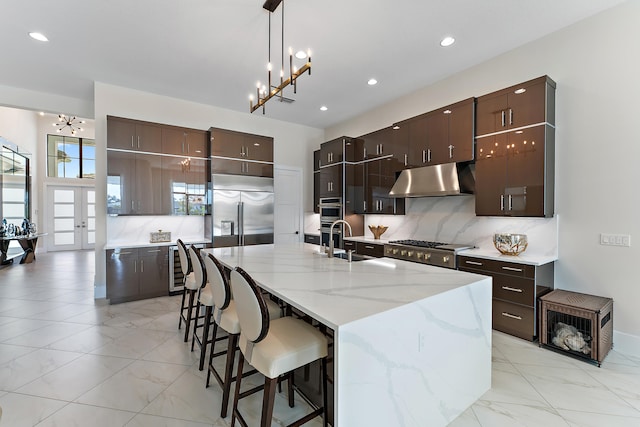 kitchen with an island with sink, sink, backsplash, appliances with stainless steel finishes, and a notable chandelier