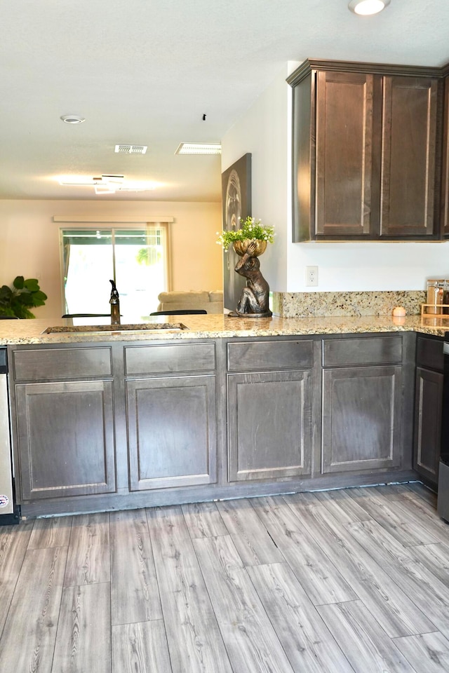 kitchen featuring light wood-type flooring, dark brown cabinetry, sink, and light stone countertops