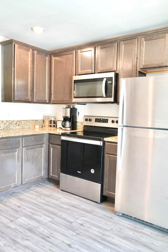 kitchen with light stone counters, light hardwood / wood-style floors, and appliances with stainless steel finishes