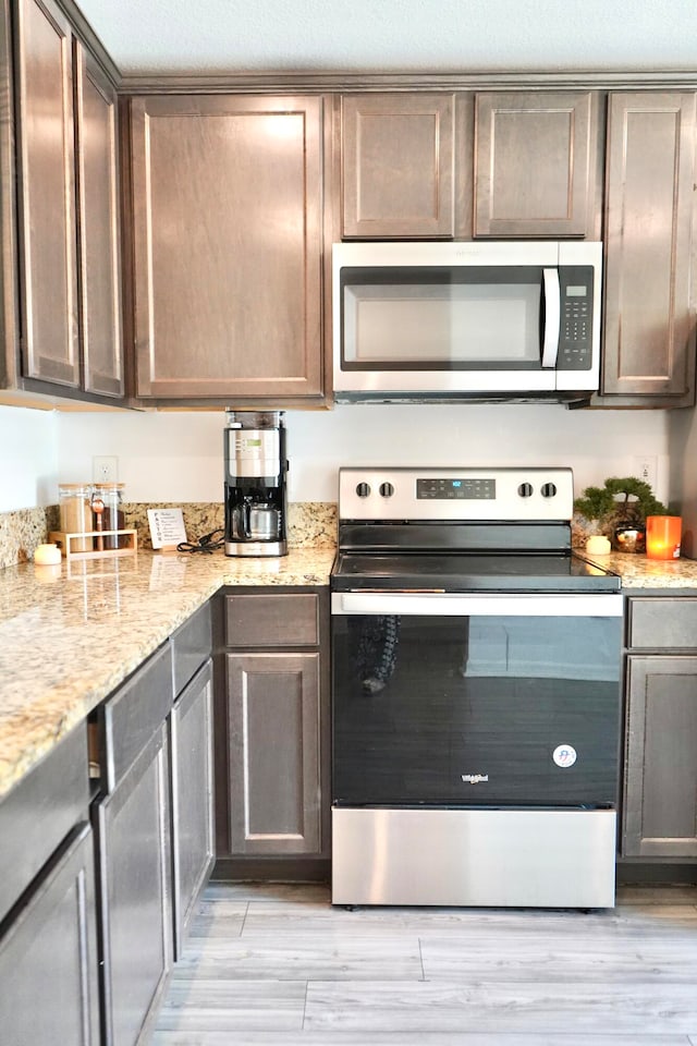 kitchen featuring dark brown cabinetry, light stone countertops, light hardwood / wood-style flooring, and stainless steel appliances