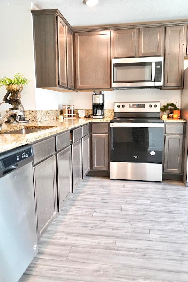 kitchen featuring light stone countertops, sink, stainless steel appliances, and light hardwood / wood-style floors