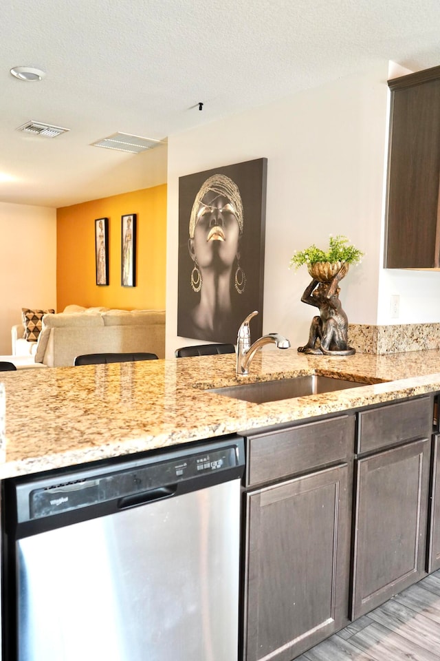 kitchen featuring light hardwood / wood-style floors, light stone counters, dark brown cabinetry, stainless steel dishwasher, and sink