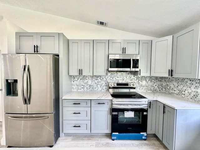 kitchen with stainless steel appliances, gray cabinets, lofted ceiling, and light hardwood / wood-style floors