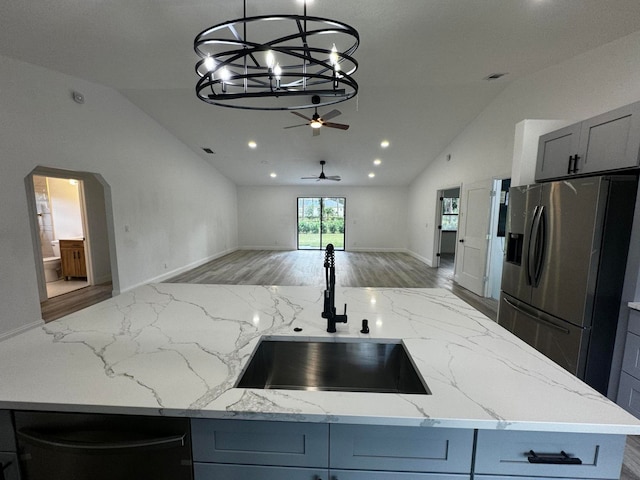 kitchen with sink, light stone counters, stainless steel fridge, gray cabinets, and ceiling fan with notable chandelier