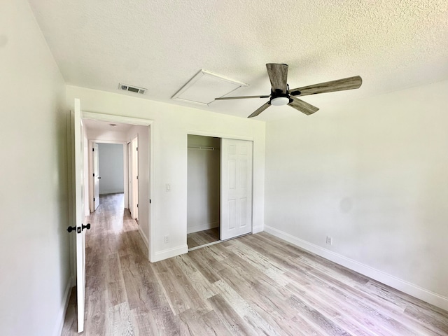 unfurnished bedroom with ceiling fan, light wood-type flooring, a textured ceiling, and a closet