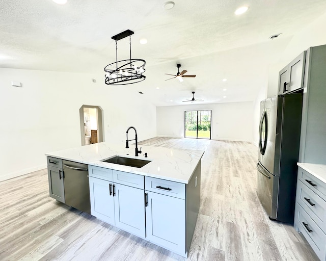 kitchen featuring sink, light hardwood / wood-style flooring, a kitchen island with sink, ceiling fan with notable chandelier, and appliances with stainless steel finishes