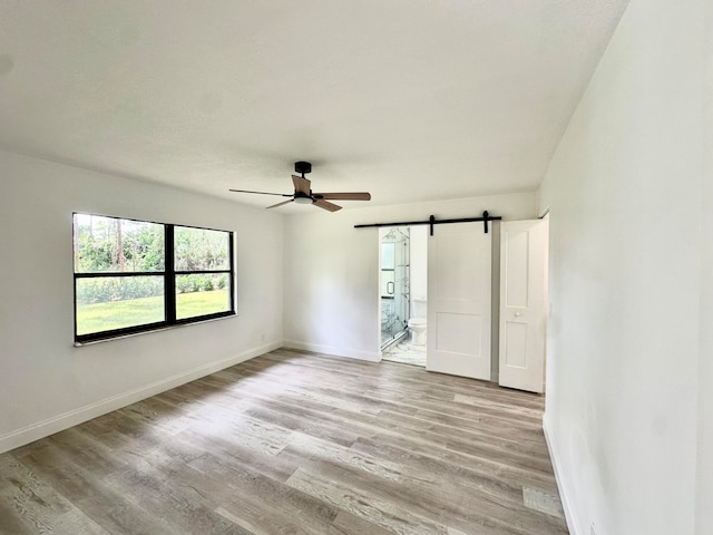 empty room with a barn door, light hardwood / wood-style floors, and ceiling fan