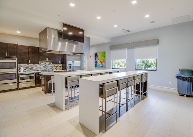 kitchen with appliances with stainless steel finishes, wall chimney range hood, a kitchen island, and a breakfast bar area