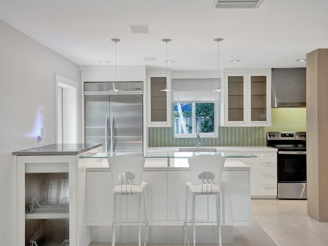 kitchen featuring appliances with stainless steel finishes, hanging light fixtures, wall chimney range hood, and white cabinets