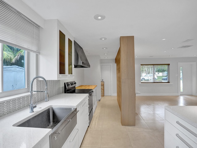 kitchen with decorative backsplash, white cabinetry, electric stove, sink, and wall chimney range hood