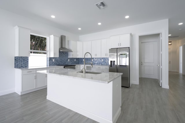 kitchen with sink, stainless steel appliances, a center island with sink, and wall chimney range hood