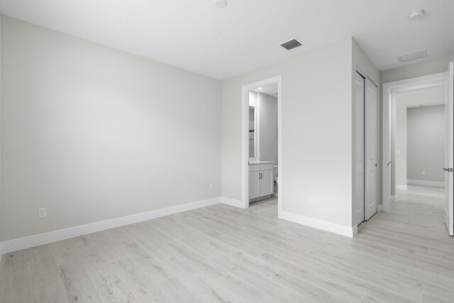 unfurnished bedroom with light hardwood / wood-style floors, ensuite bath, and a closet