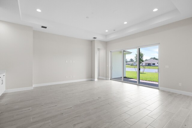 empty room featuring light wood-type flooring and a tray ceiling