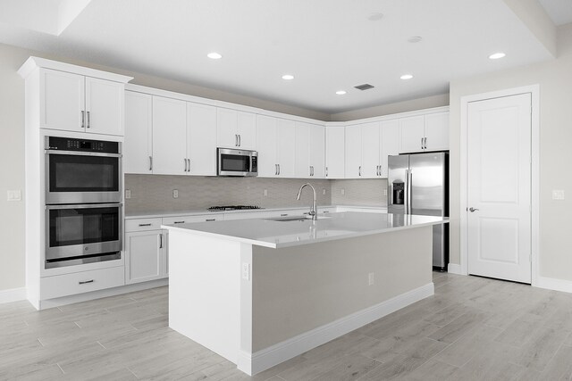 kitchen featuring stainless steel appliances, white cabinets, a kitchen island with sink, and sink