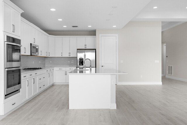 kitchen with a kitchen island with sink, sink, white cabinetry, light hardwood / wood-style flooring, and appliances with stainless steel finishes