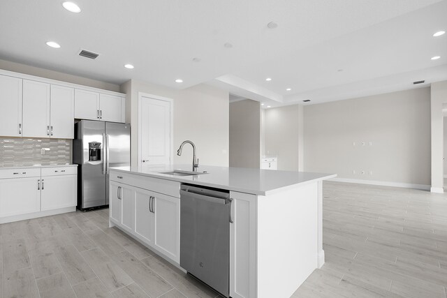 kitchen with appliances with stainless steel finishes, light hardwood / wood-style floors, white cabinets, a kitchen island with sink, and sink