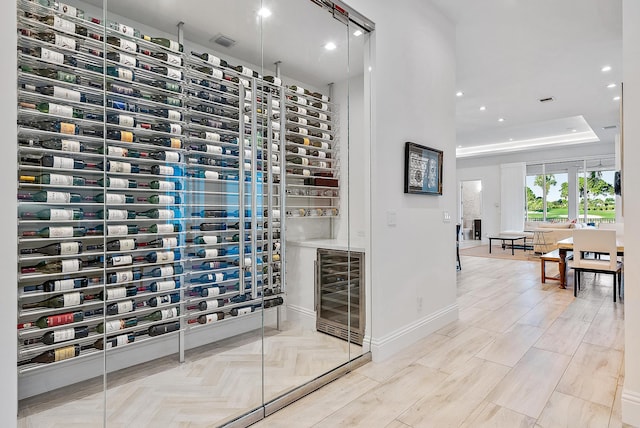 wine area with beverage cooler, a raised ceiling, and light hardwood / wood-style floors