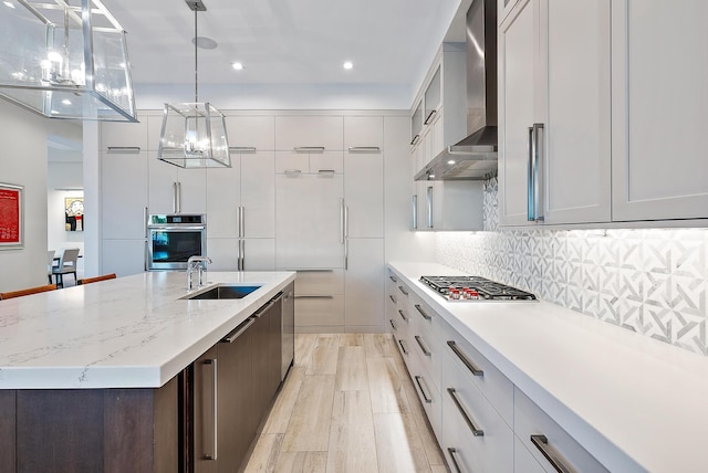 kitchen with wall chimney exhaust hood, stainless steel appliances, light hardwood / wood-style floors, and hanging light fixtures