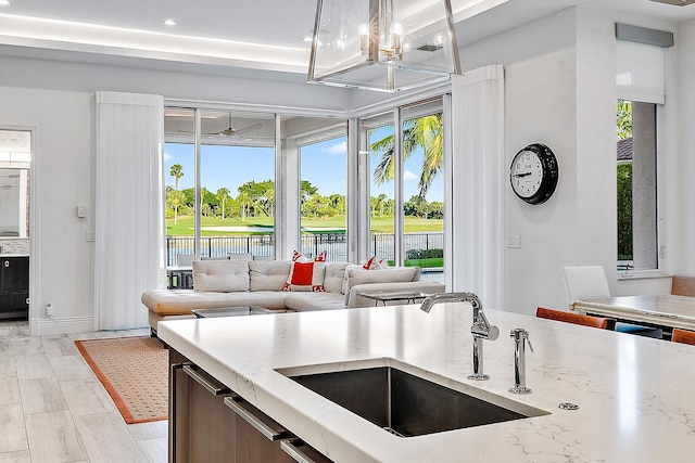 kitchen with light stone counters, pendant lighting, sink, light wood-type flooring, and a water view