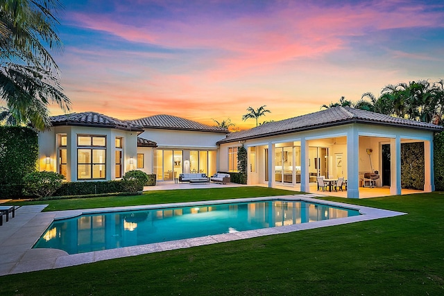 back house at dusk featuring a lawn, an outdoor living space, ceiling fan, and a patio area