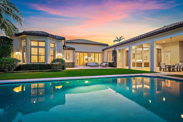 back house at dusk featuring a patio, outdoor lounge area, and a yard