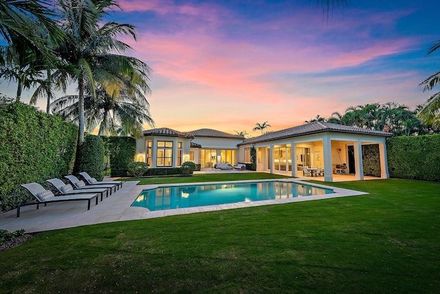 pool at dusk featuring a yard and a patio