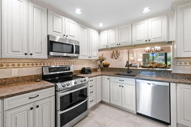 kitchen with dark stone counters, an inviting chandelier, white cabinets, sink, and stainless steel appliances