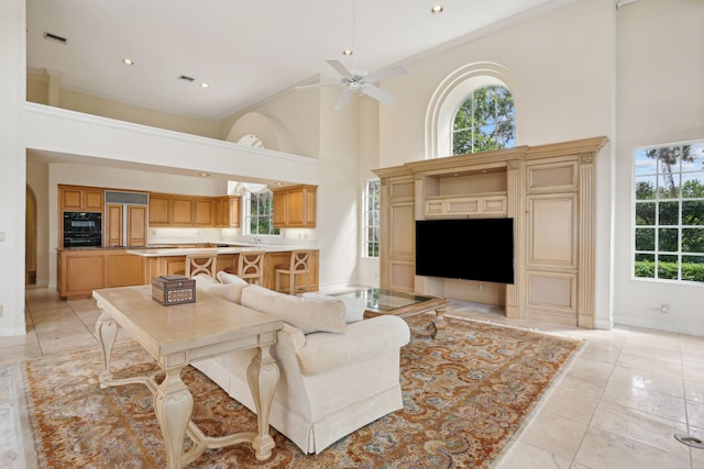 living room featuring ceiling fan, crown molding, light tile patterned floors, and a high ceiling