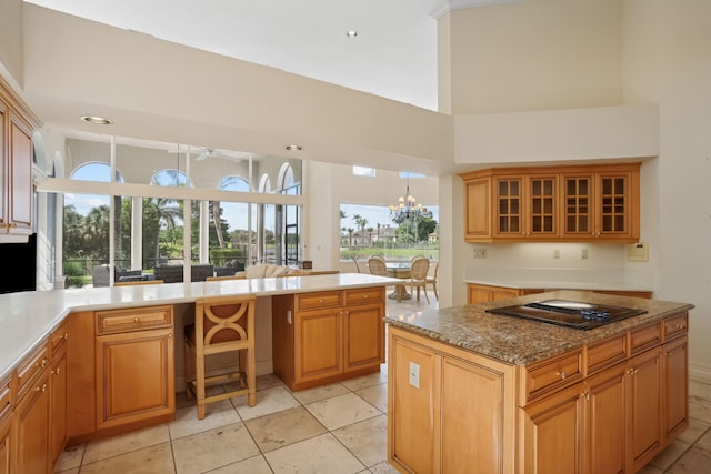 kitchen featuring light stone countertops, a towering ceiling, an inviting chandelier, hanging light fixtures, and black stovetop