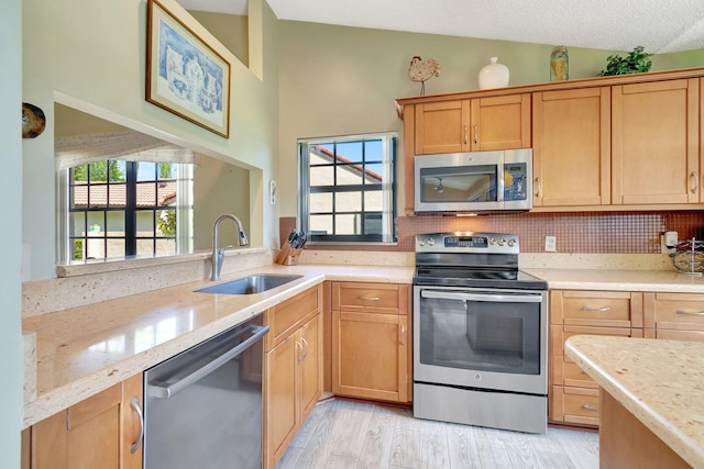 kitchen with appliances with stainless steel finishes, light hardwood / wood-style floors, vaulted ceiling, a textured ceiling, and sink