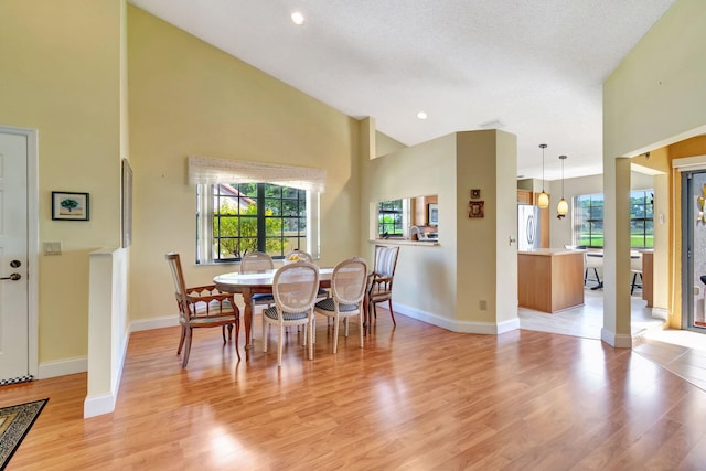 dining room with a textured ceiling, light hardwood / wood-style floors, and high vaulted ceiling