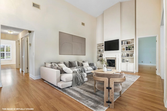 living room featuring built in features, light wood-type flooring, and a towering ceiling