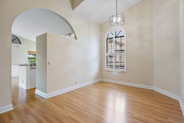 spare room with light hardwood / wood-style floors, a textured ceiling, vaulted ceiling, and an inviting chandelier