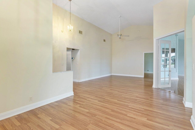 empty room featuring high vaulted ceiling, ceiling fan with notable chandelier, and light wood-type flooring