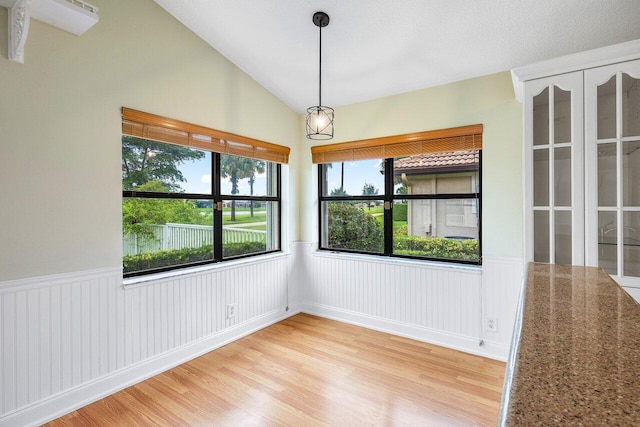 spare room featuring light wood-type flooring, lofted ceiling, and a textured ceiling