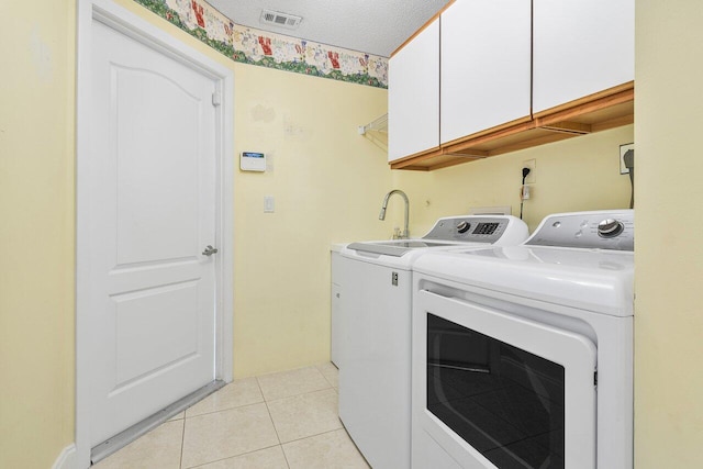 clothes washing area with a textured ceiling, separate washer and dryer, cabinets, and light tile patterned floors