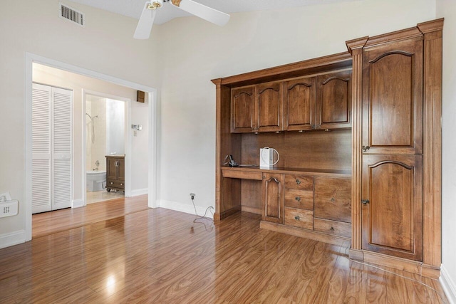unfurnished office with vaulted ceiling, built in desk, ceiling fan, and light hardwood / wood-style flooring