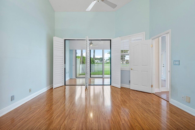 empty room with a towering ceiling, ceiling fan, and light wood-type flooring