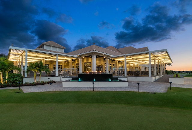 back house at dusk featuring a patio area, a yard, a swimming pool with hot tub, and pool water feature