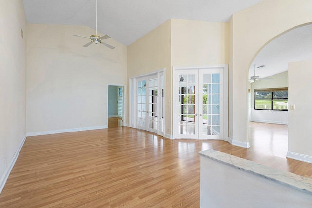 unfurnished living room with french doors, light hardwood / wood-style floors, ceiling fan, and high vaulted ceiling