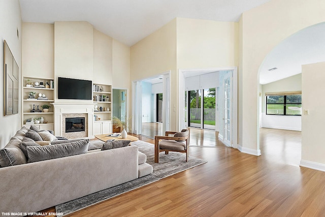 living room featuring built in shelves, high vaulted ceiling, and light hardwood / wood-style flooring