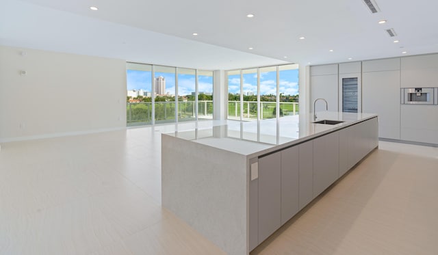 kitchen with floor to ceiling windows, gray cabinetry, sink, and a spacious island