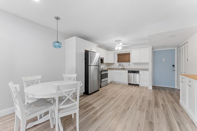 kitchen featuring decorative light fixtures, stainless steel appliances, light hardwood / wood-style floors, and white cabinetry