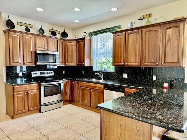 kitchen featuring light tile patterned flooring, kitchen peninsula, stainless steel appliances, dark stone counters, and sink