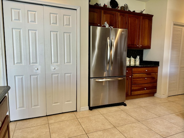 kitchen with dark stone counters, stainless steel fridge, and light tile patterned floors