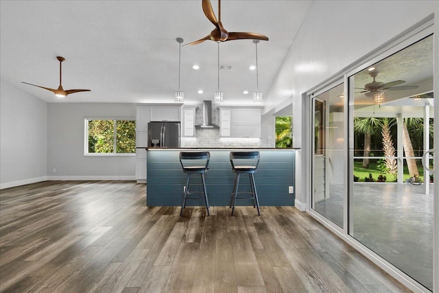 kitchen with stainless steel refrigerator with ice dispenser, hardwood / wood-style floors, wall chimney range hood, and white cabinetry