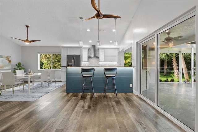 kitchen featuring wall chimney exhaust hood, hardwood / wood-style floors, stainless steel fridge with ice dispenser, and white cabinetry