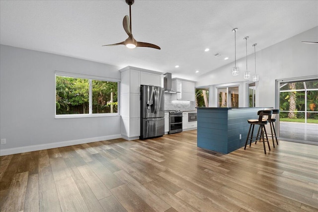 kitchen featuring light hardwood / wood-style floors, wall chimney range hood, a breakfast bar area, appliances with stainless steel finishes, and white cabinetry