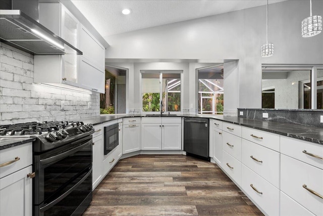 kitchen featuring wall chimney range hood, vaulted ceiling, black appliances, and dark stone countertops